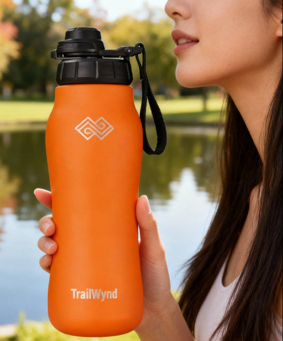 Person holding an orange TrailWynd water bottle by a lake